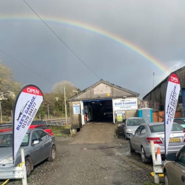 A rainbow over the Blee's Garage workshop, with Blee's Garage flags and an Open flag in the yard